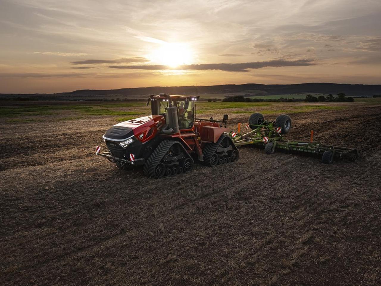 Red tractor on a field with a sunset behind it