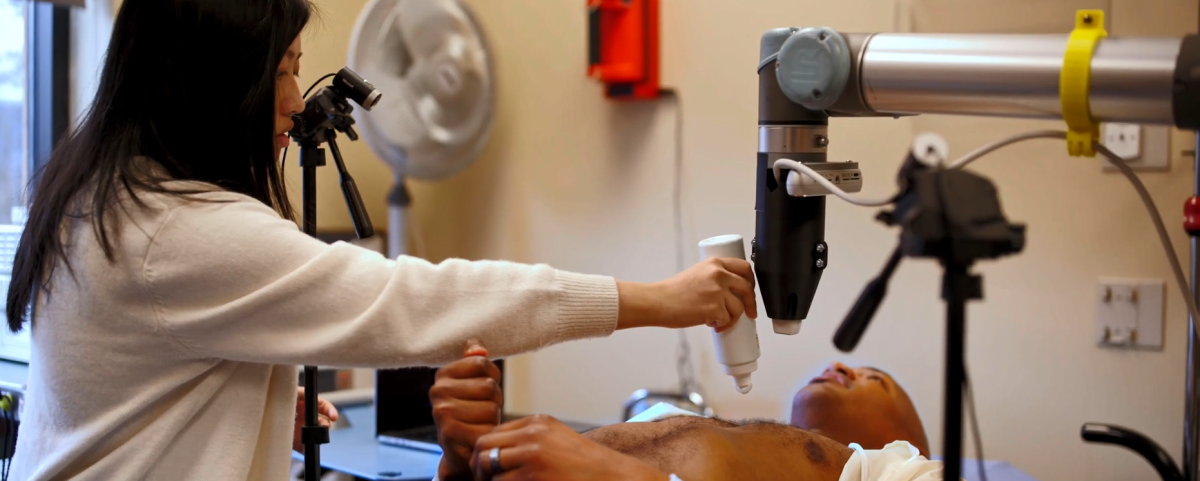 A person laying down receiving an ultrasound, a medical professional applying gel to their chest.