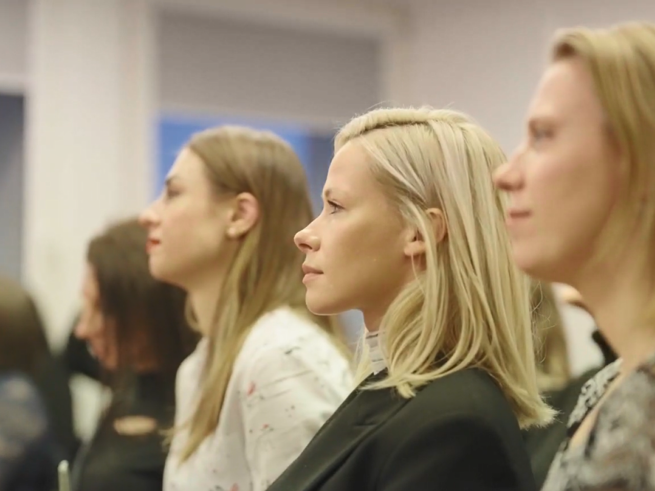 Seated people in a room of others, looking in the same direction.